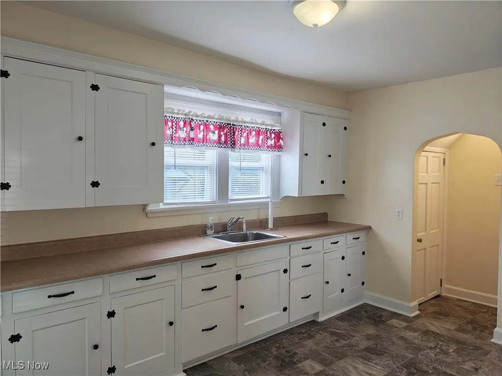 Kitchen featuring white cabinetry, arched walkways, and light countertops