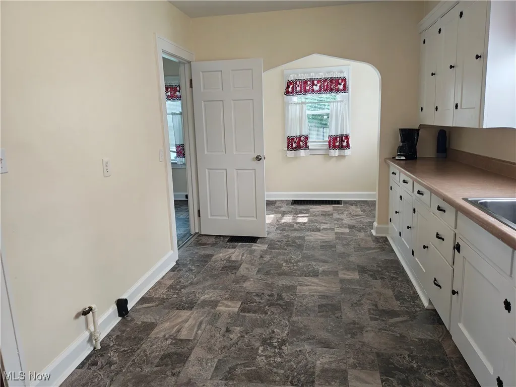 Kitchen with white cabinetry, arched walkways, and stone finish flooring