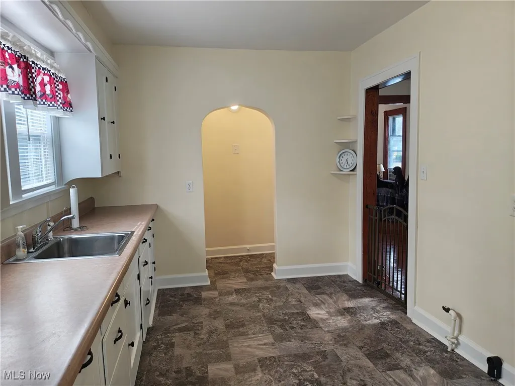 Kitchen with arched walkways, white cabinetry, light countertops, and stone finish floors