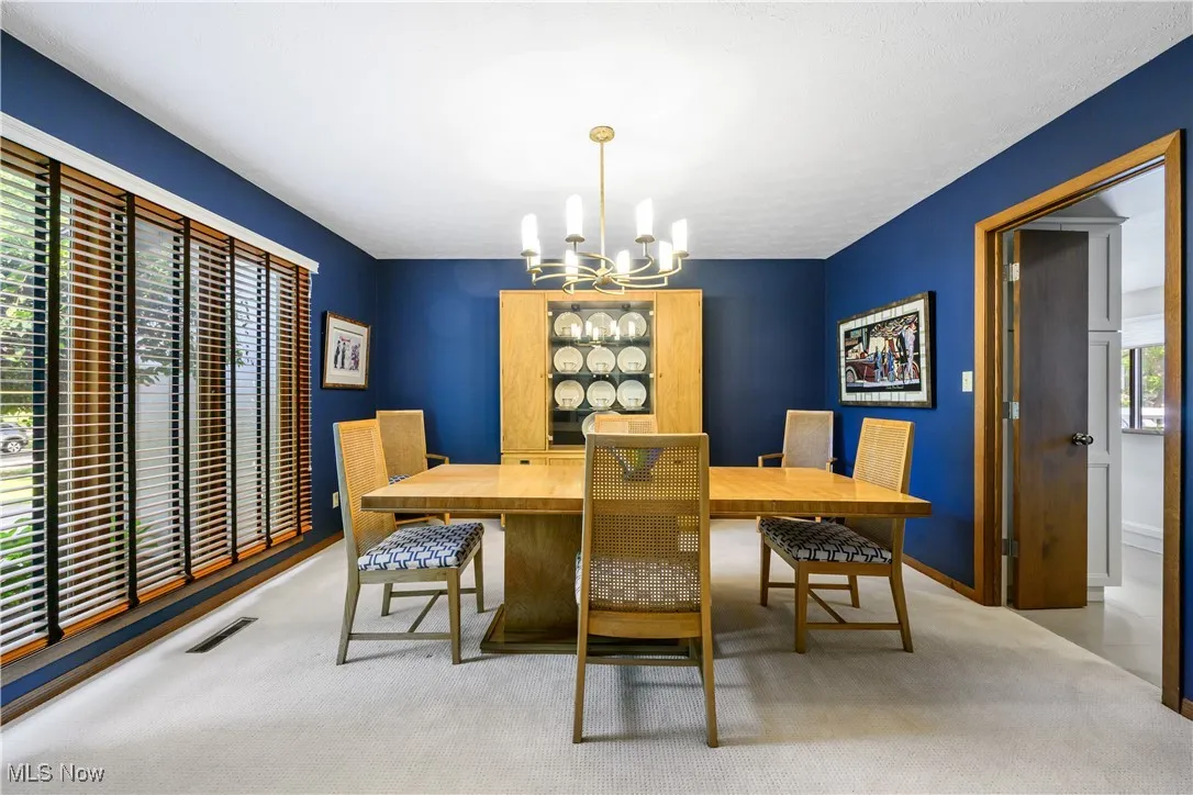 Carpeted dining space with a chandelier and baseboards
