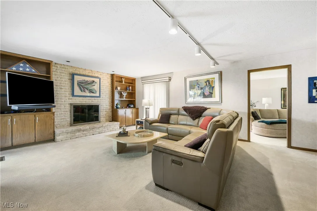 Living area featuring carpet, a brick fireplace, a textured ceiling, rail lighting, and built in features