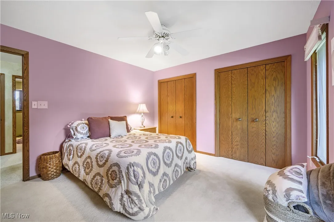 Bedroom featuring light colored carpet, multiple closets, and ceiling fan