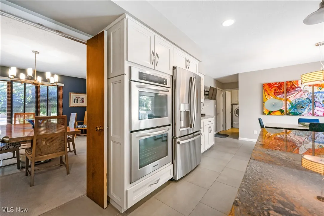 Kitchen with a chandelier, stainless steel appliances, white cabinetry, light tile patterned flooring, and hanging light fixtures