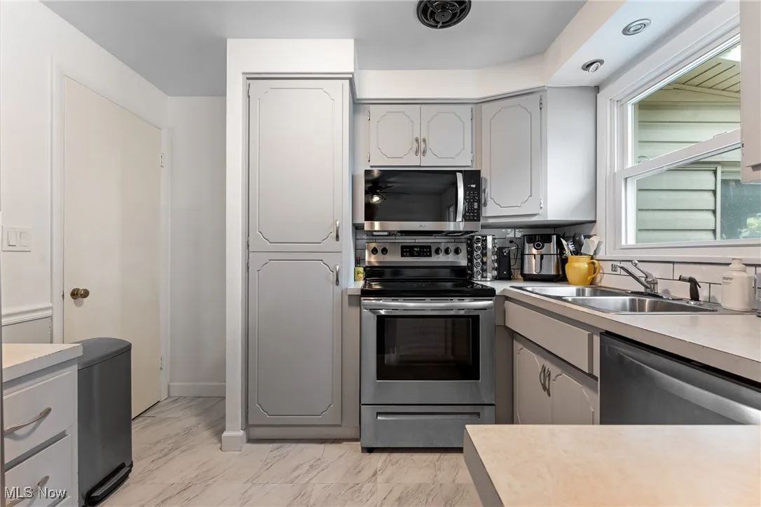 Kitchen with appliances with stainless steel finishes, light countertops, gray cabinets, and light marble finish flooring