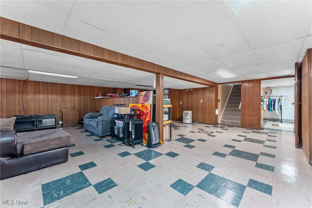 Finished below grade area featuring a paneled ceiling, stairway, wood walls, and tile patterned floors