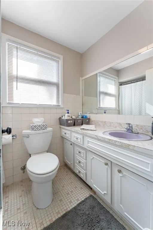Full bathroom with tile patterned floors, tile walls, vanity, a wainscoted wall, and a shower with curtain
