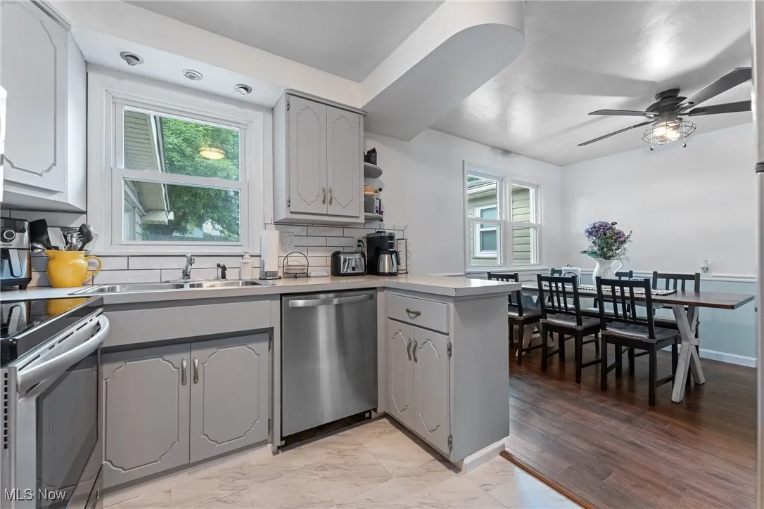 Kitchen featuring gray cabinetry, a peninsula, dishwasher, backsplash, and a ceiling fan