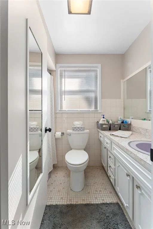 Bathroom featuring tile walls, tile patterned flooring, vanity, a shower with curtain, and wainscoting