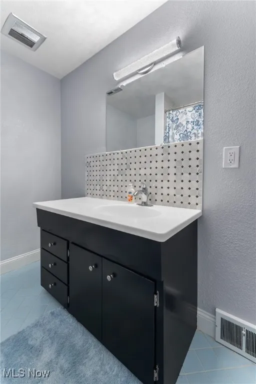 Full bath with vanity, a textured wall, and tile patterned floors