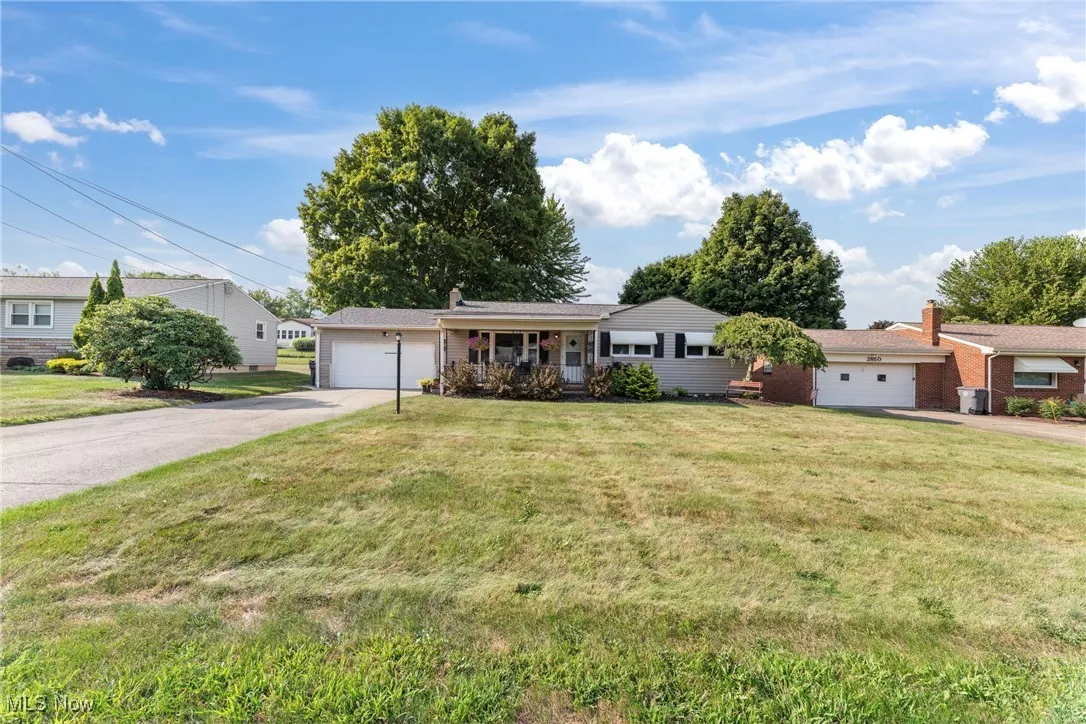 Ranch-style house featuring an attached garage, driveway, a front lawn, and a porch