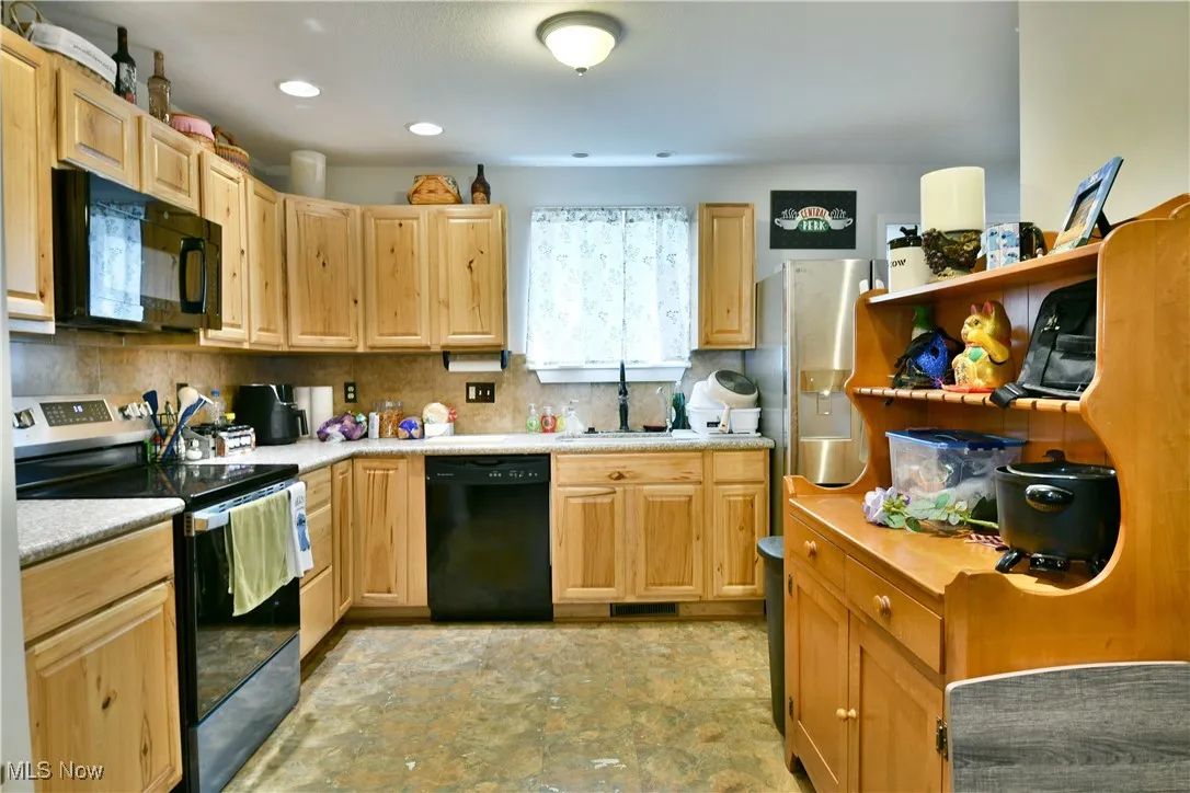 Kitchen featuring black appliances, light brown cabinetry, light countertops, backsplash, and open shelves