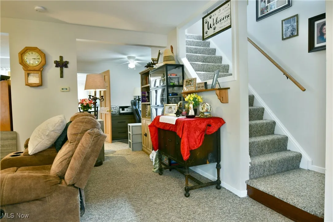 Carpeted living area with stairs and ceiling fan