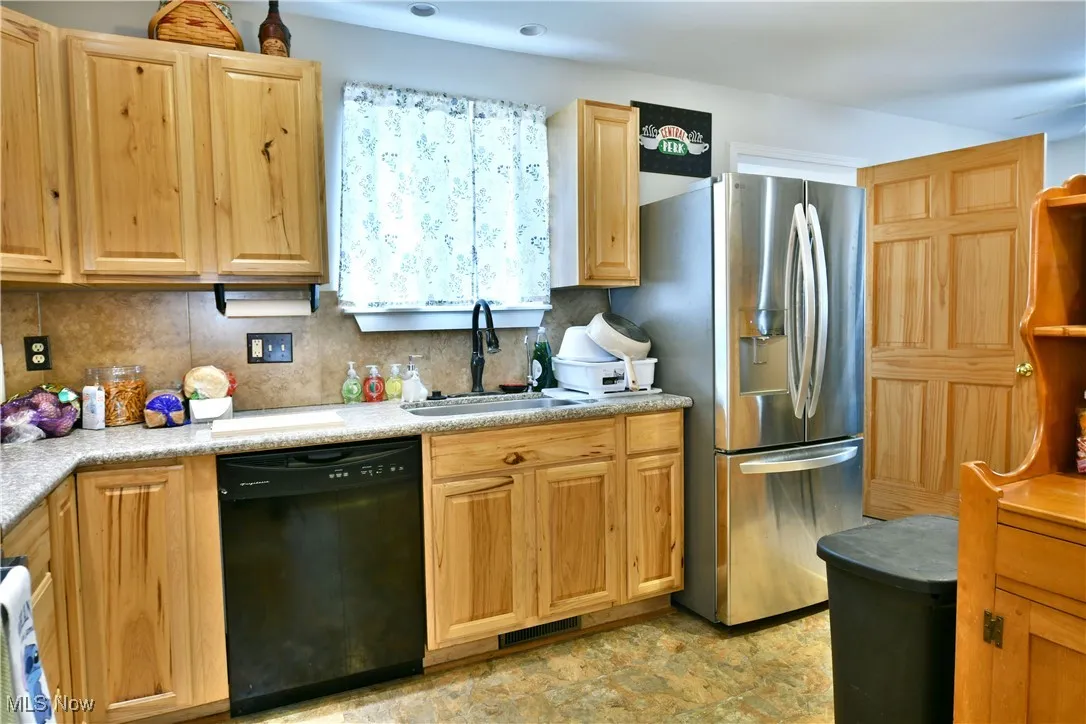 Kitchen featuring dishwasher, stainless steel refrigerator with ice dispenser, backsplash, light countertops, and light brown cabinets