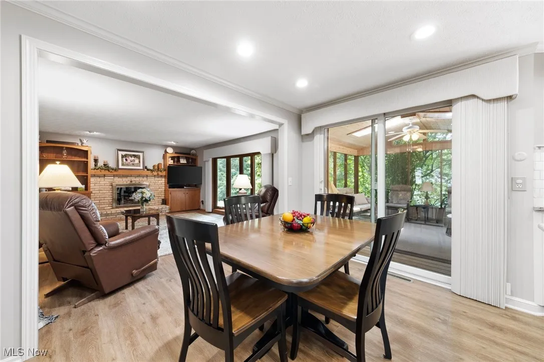 Dining room with a fireplace, light wood finished floors, ornamental molding, recessed lighting, and ceiling fan