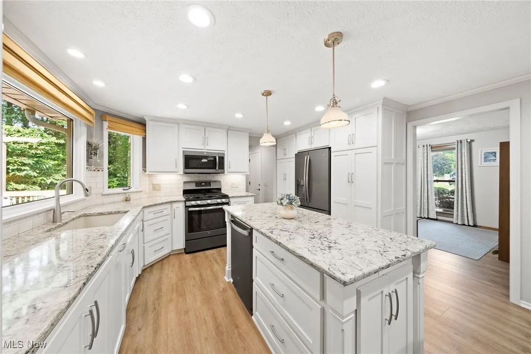 Kitchen with a center island, stainless steel appliances, decorative backsplash, white cabinetry, and light wood-type flooring