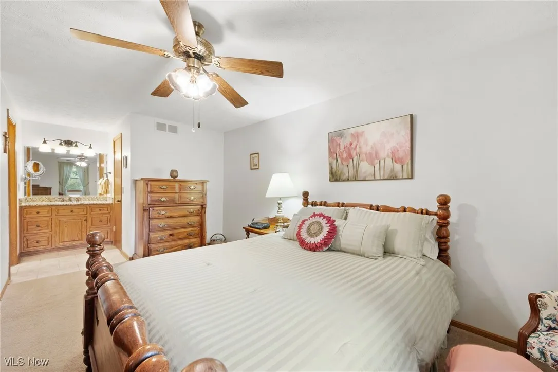 Bedroom with ensuite bath, light carpet, and ceiling fan