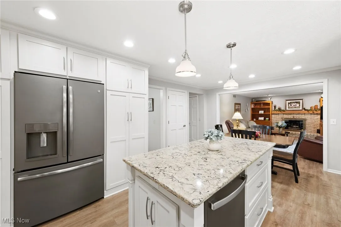 Kitchen featuring stainless steel appliances, light wood finished floors, white cabinetry, a brick fireplace, and light stone countertops