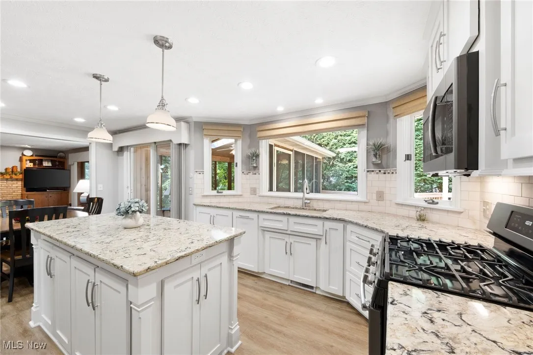 Kitchen with range with gas stovetop, tasteful backsplash, white cabinets, a kitchen island, and stainless steel microwave