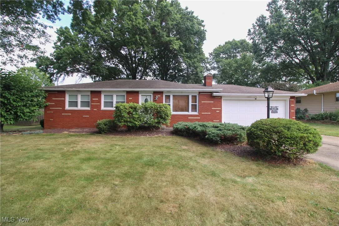 Ranch-style home featuring a garage, a chimney, a front lawn, brick siding, and concrete driveway