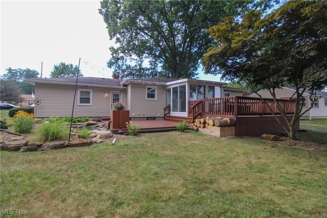 Rear view of house featuring a deck, a sunroom, and a lawn