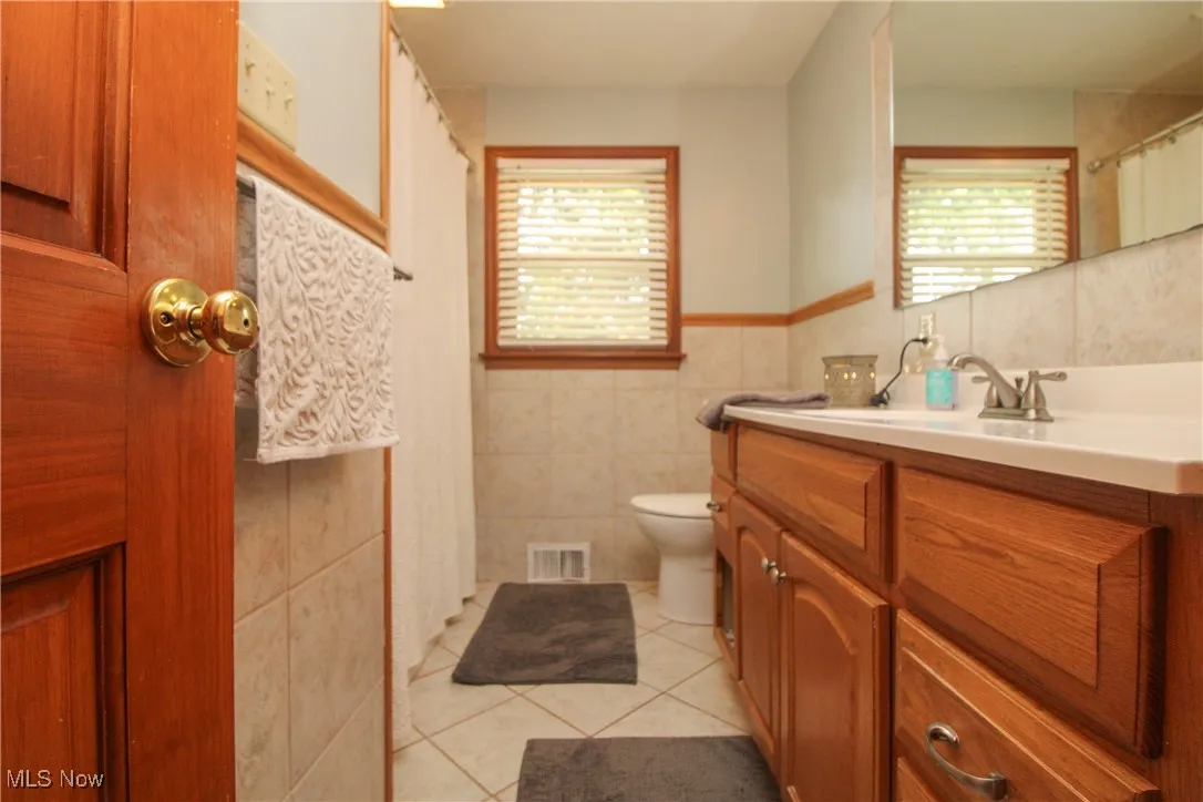 Bathroom featuring tile walls, healthy amount of natural light, tile patterned floors, vanity, and a wainscoted wall