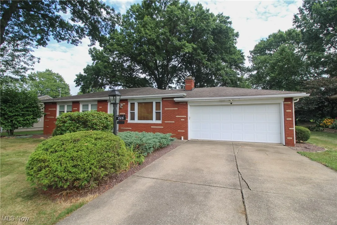Ranch-style home featuring an attached garage, brick siding, a chimney, and concrete driveway