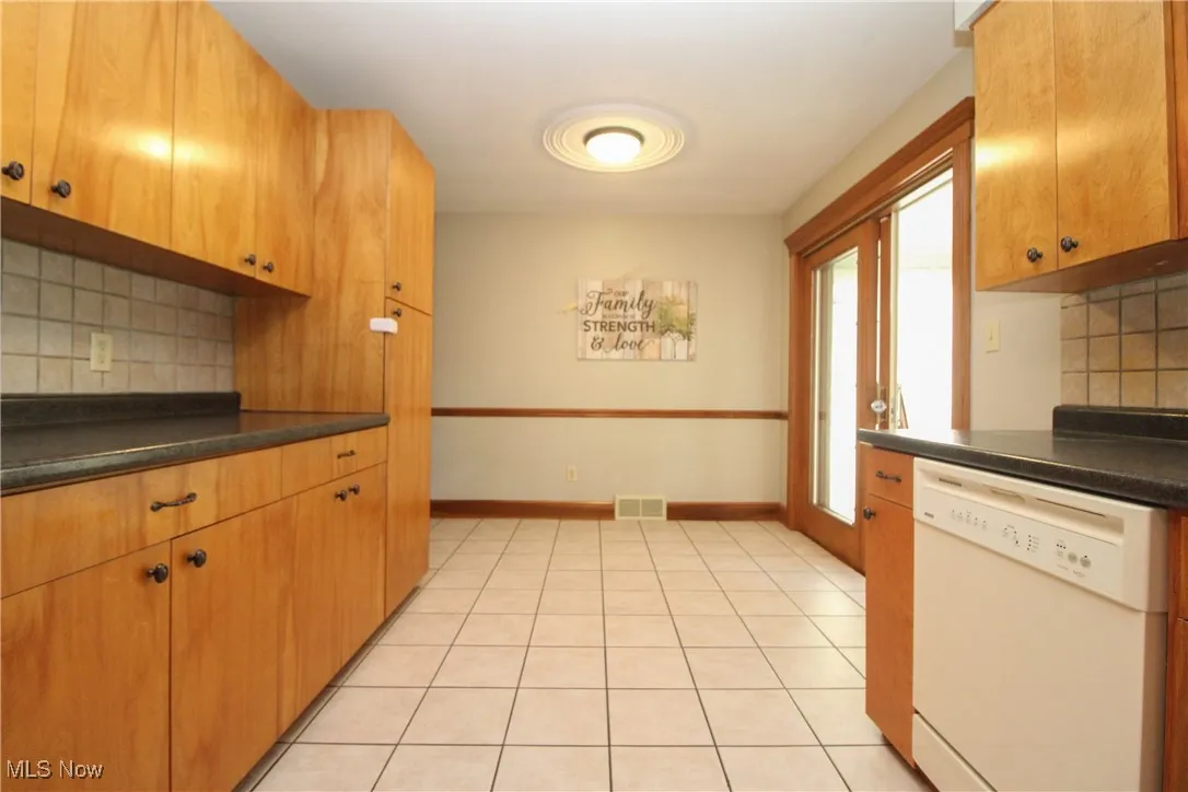 Kitchen with decorative backsplash, white dishwasher, dark countertops, and light tile patterned flooring
