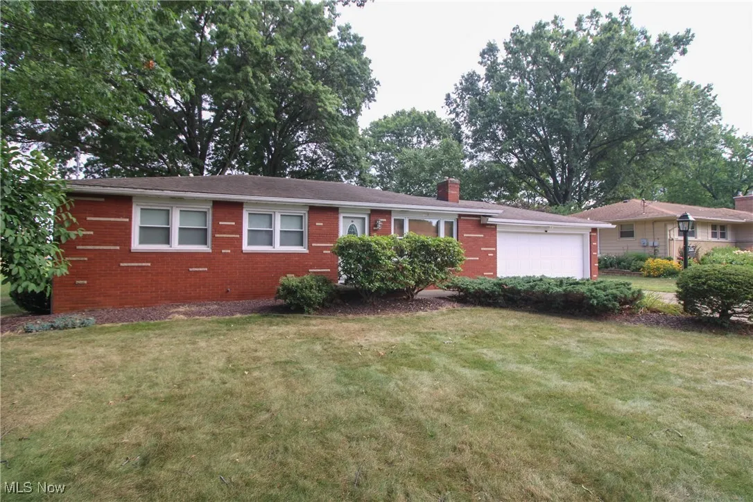 Single story home with an attached garage, a chimney, brick siding, and a front yard