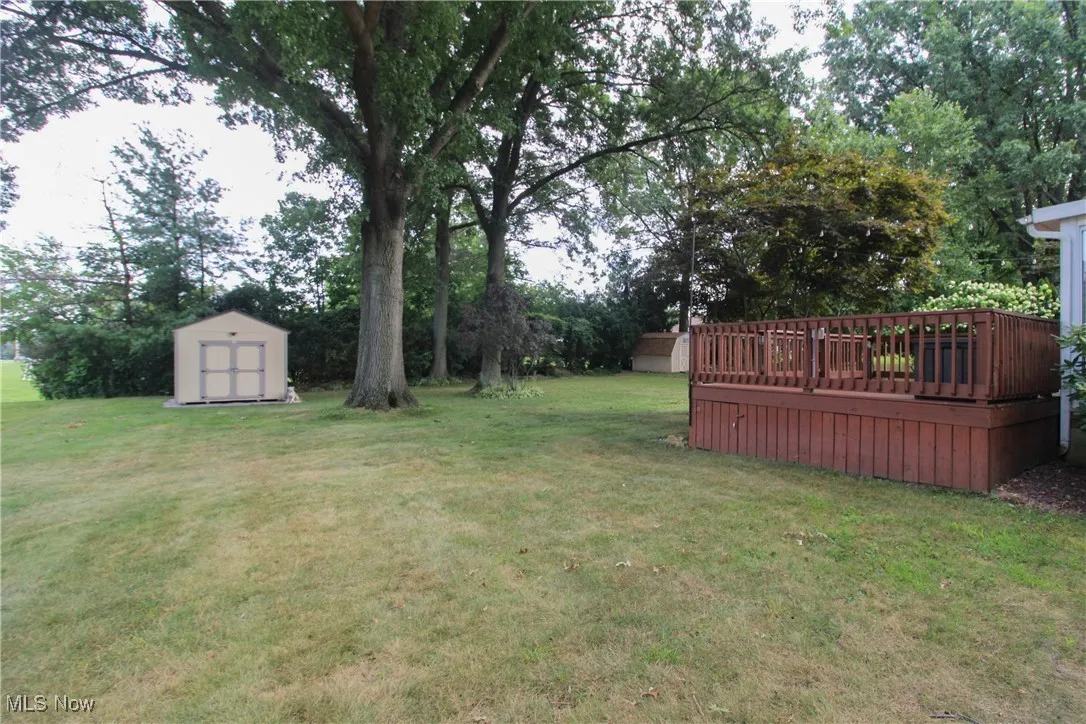 View of grassy yard featuring a storage unit and a wooden deck