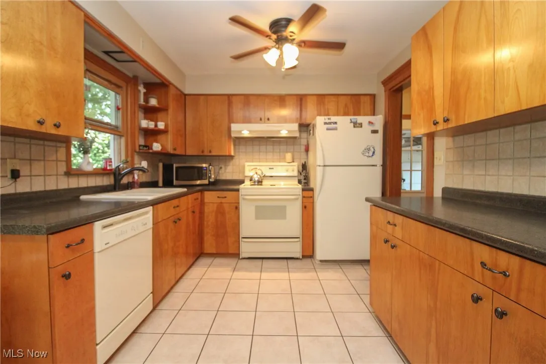 Kitchen featuring white appliances, backsplash, dark countertops, and light tile patterned floors