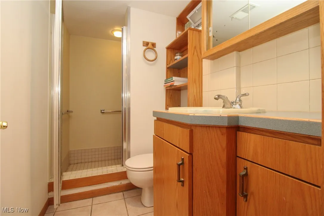 Bathroom featuring vanity, tile patterned floors, a stall shower, and backsplash