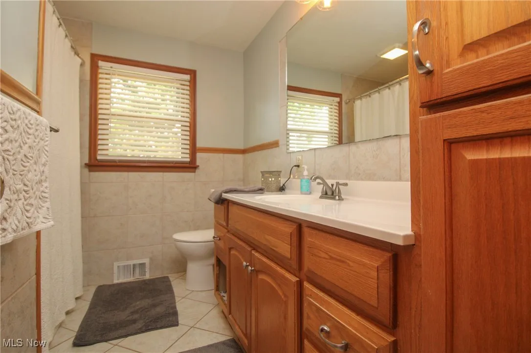 Full bath featuring tile walls, tile patterned floors, vanity, and a wainscoted wall