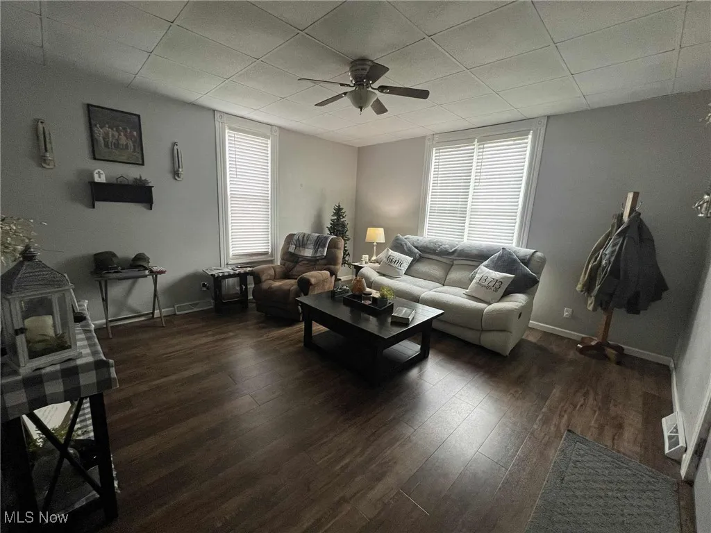Living area featuring ceiling fan, wood finished floors, plenty of natural light, a wood stove, and a drop ceiling