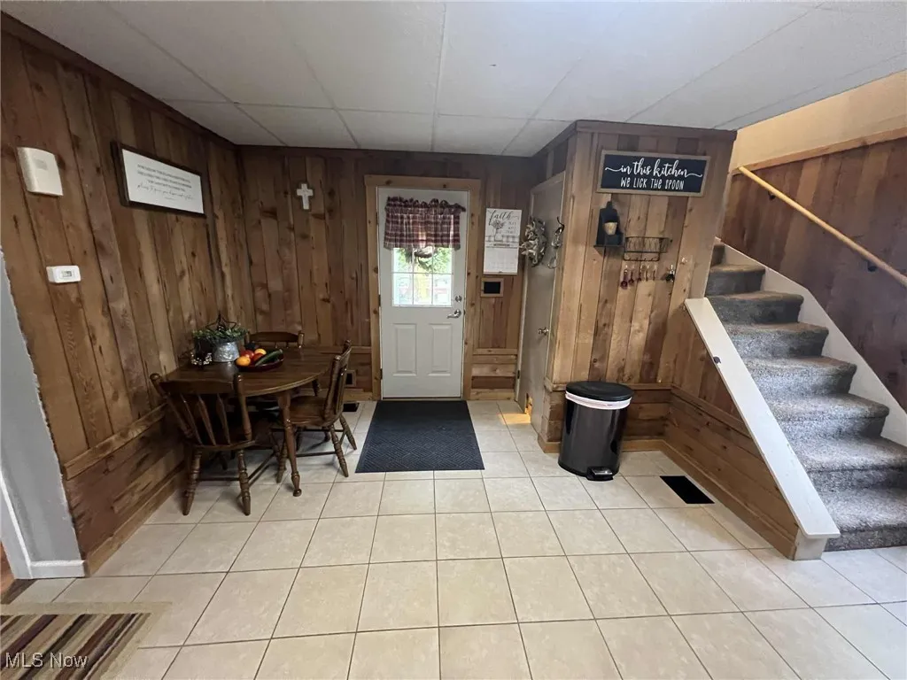 Entryway with stairway, wooden walls, and light tile patterned floors