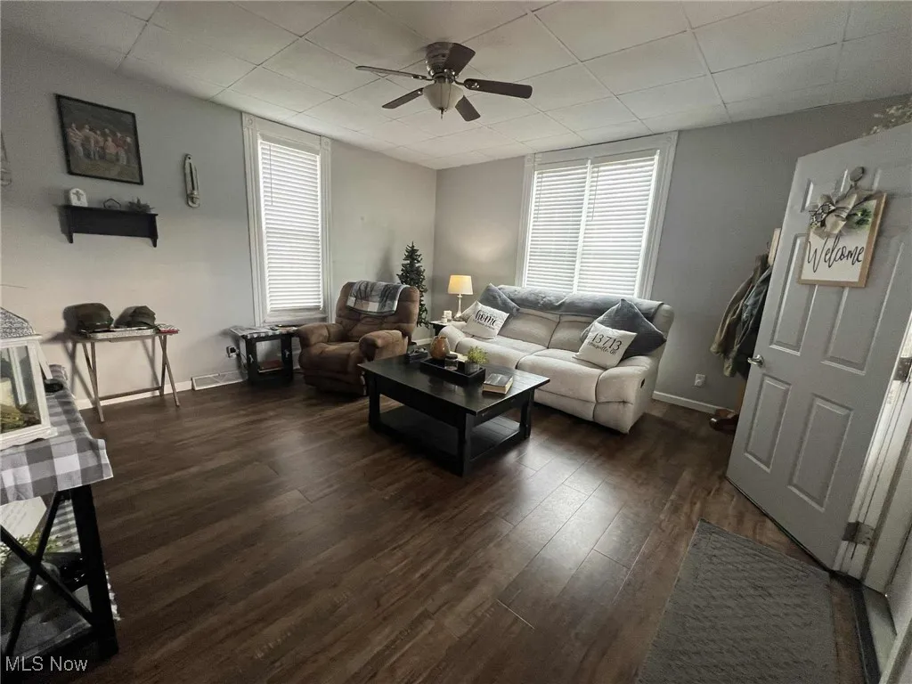 Living room featuring a ceiling fan, dark wood-style floors, and a paneled ceiling