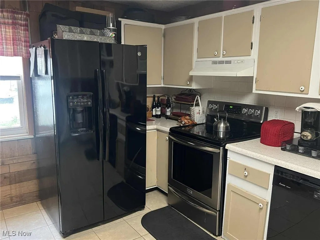 Kitchen with black appliances, light countertops, under cabinet range hood, and light tile patterned floors
