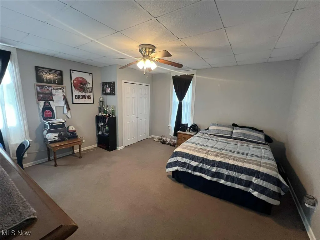 Bedroom featuring a paneled ceiling, dark carpet, a ceiling fan, and a closet
