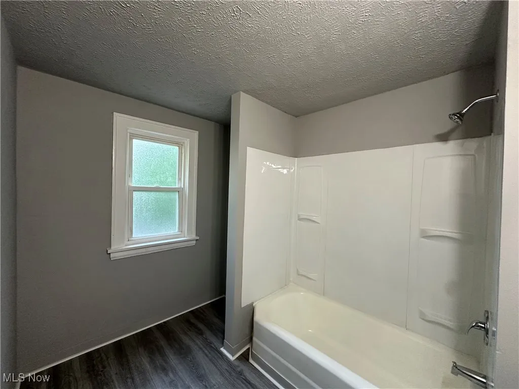 Bathroom with a textured ceiling, washtub / shower combination, and wood finished floors