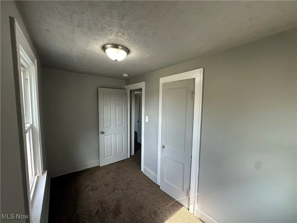 Unfurnished bedroom featuring dark colored carpet and a textured ceiling