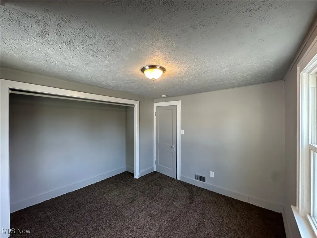 Unfurnished bedroom featuring dark colored carpet, a textured ceiling, and a closet