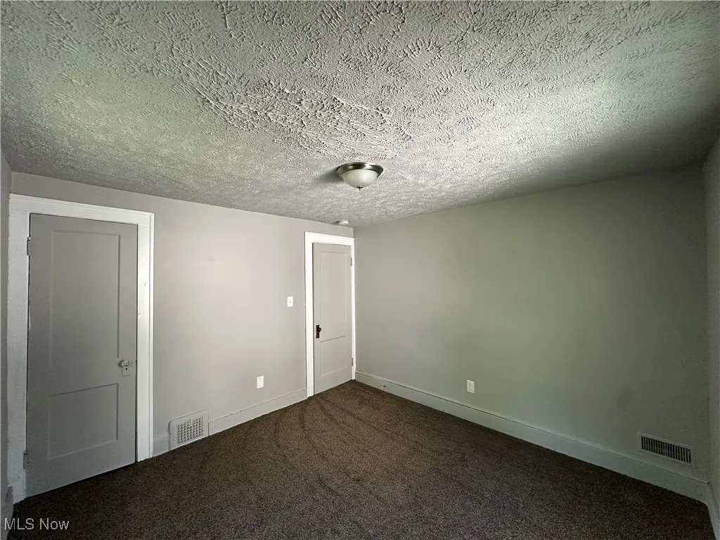 Unfurnished bedroom featuring dark carpet and a textured ceiling