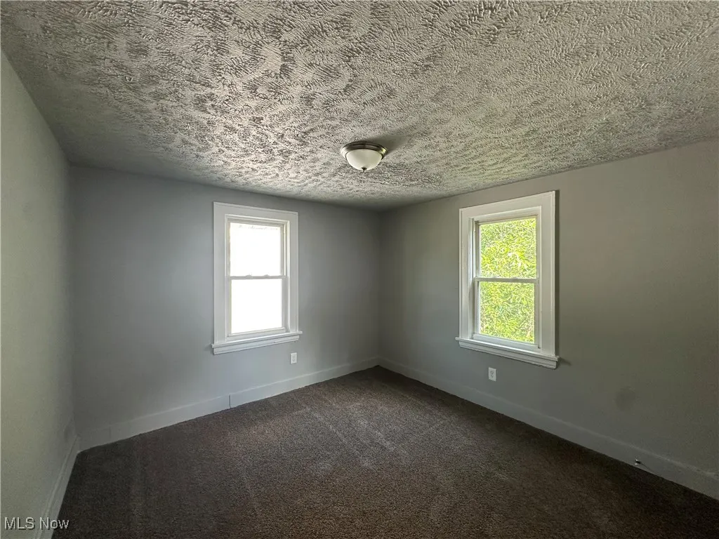Unfurnished room with dark colored carpet, healthy amount of natural light, and a textured ceiling