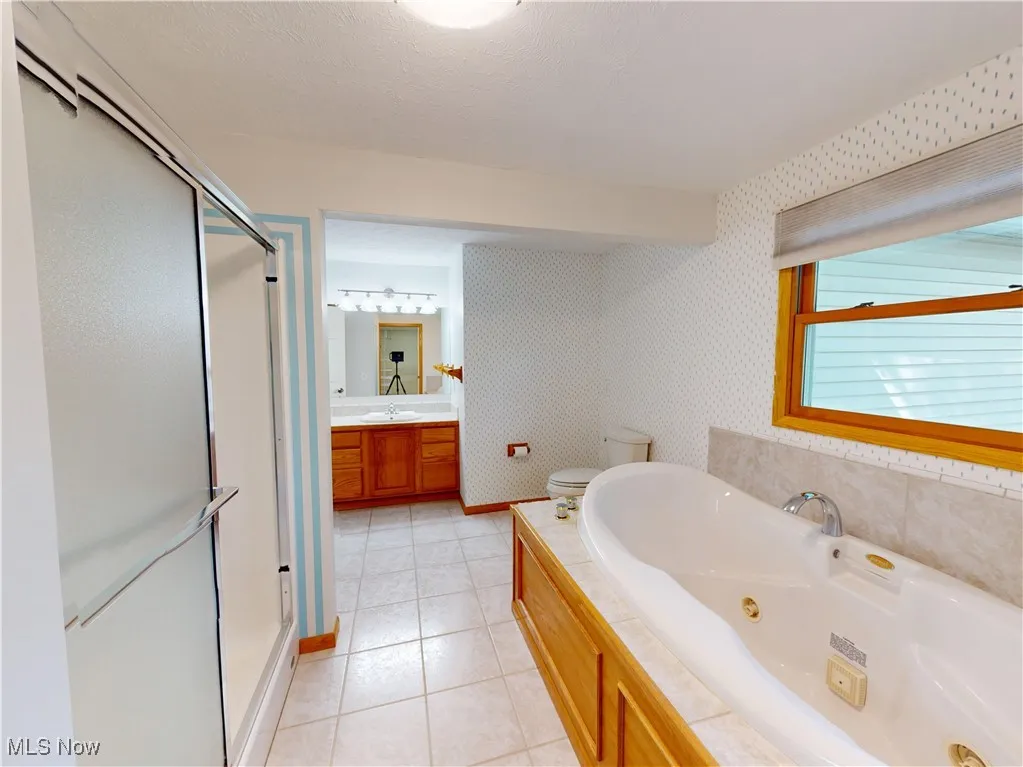 Bathroom with a shower stall, vanity, a jetted tub, light tile patterned floors, and wallpapered walls
