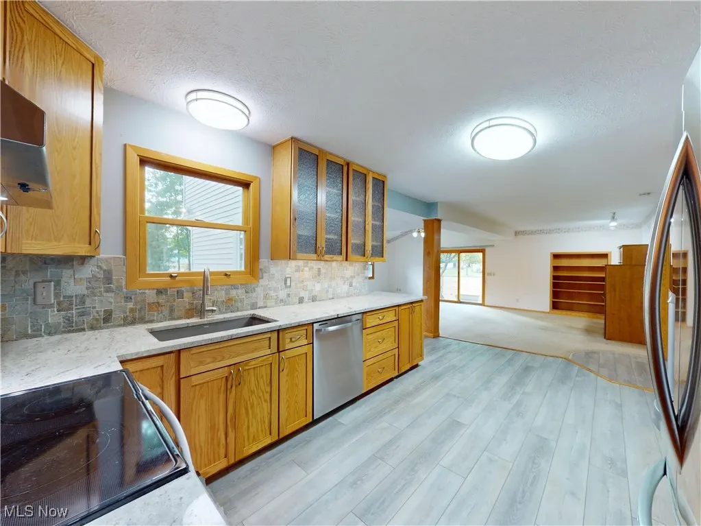Kitchen with tasteful backsplash, light stone counters, stainless steel appliances, glass insert cabinets, and light wood finished floors