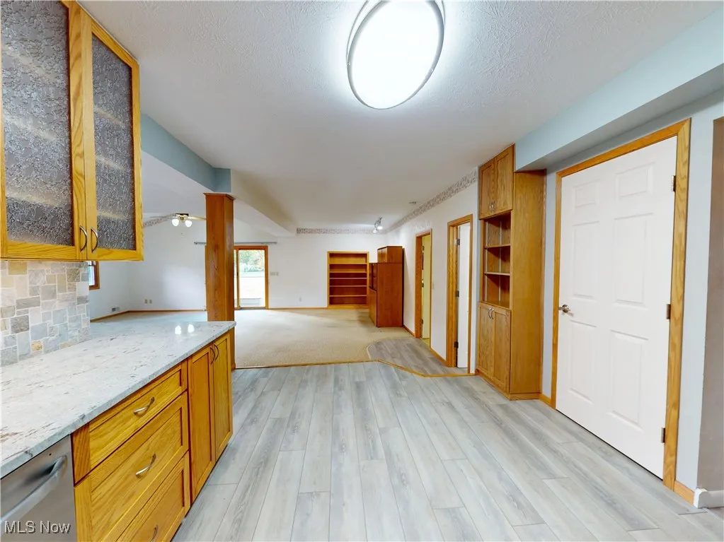 Kitchen featuring glass insert cabinets, brown cabinets, light stone counters, light wood-style flooring, and a textured ceiling