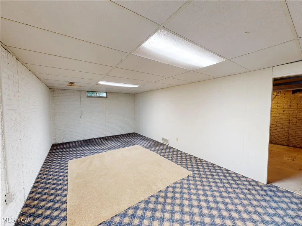 Below grade area with brick wall, a drop ceiling, and carpet