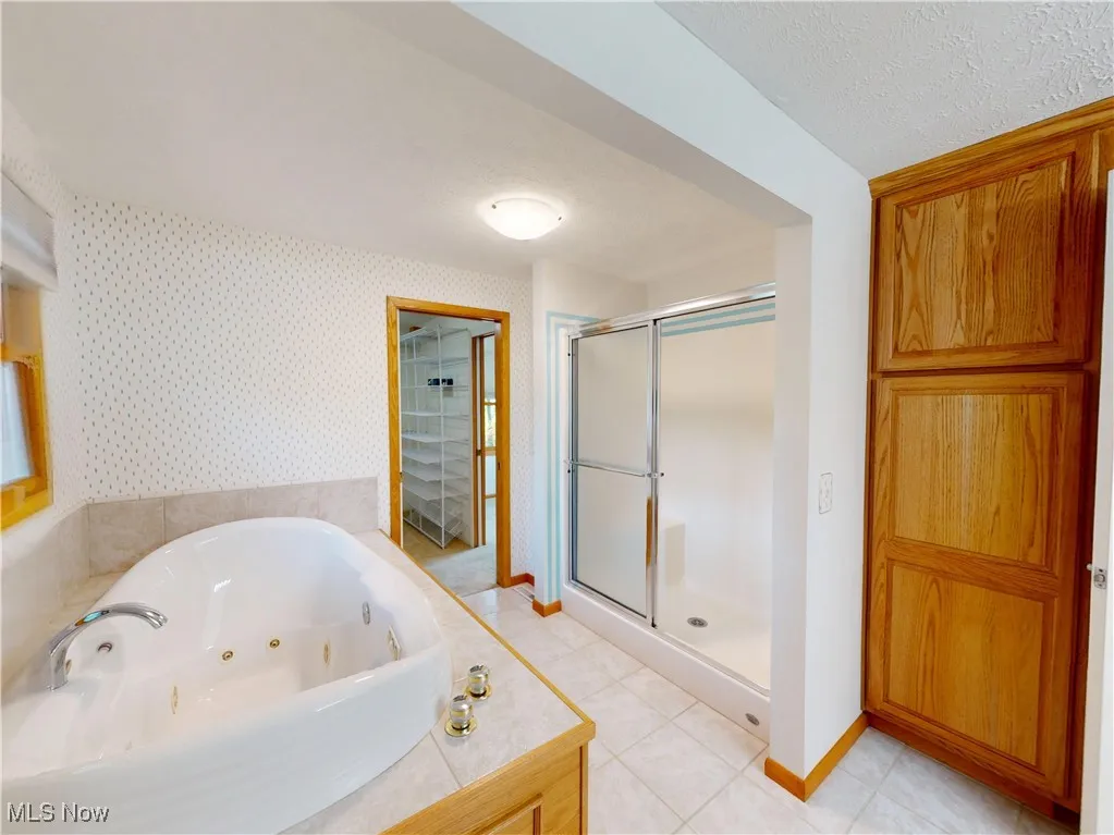 Full bathroom featuring a shower stall, a whirlpool tub, light tile patterned floors, a textured ceiling, and wallpapered walls