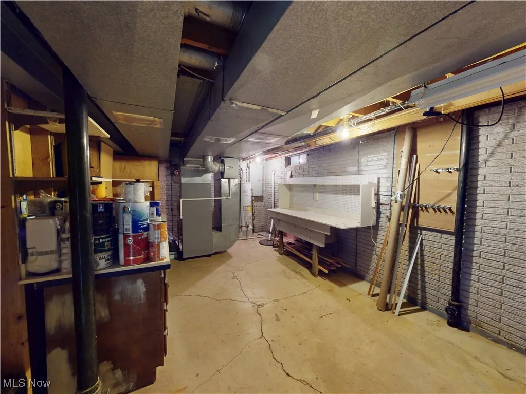 Unfinished below grade area with heating unit, electric panel, and water heater