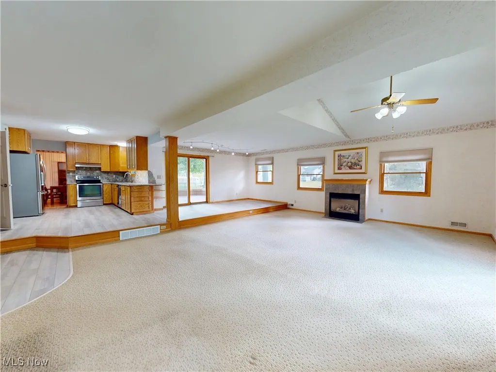  living room featuring a ceiling fan, a fireplace, track lighting, and light colored carpet