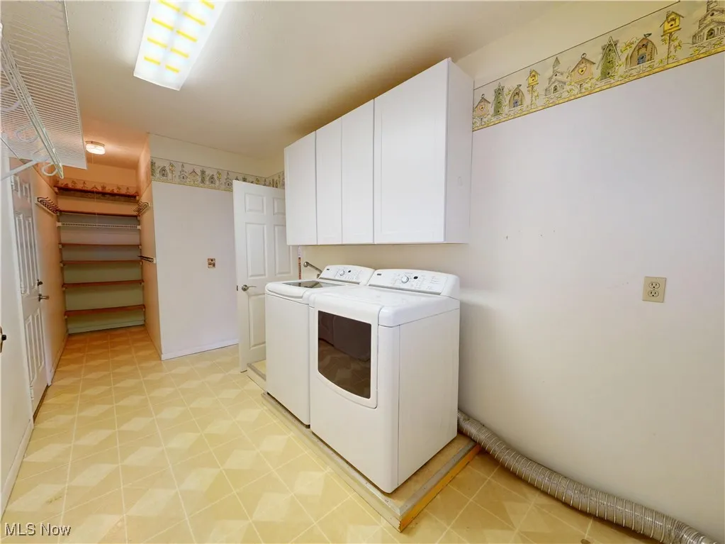 Washroom with cabinet space, washer and clothes dryer, and light floors